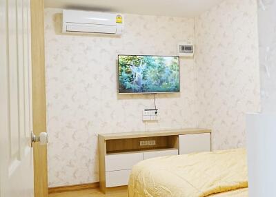 Modern bedroom with a bed, wall-mounted TV, air conditioner, and wooden flooring