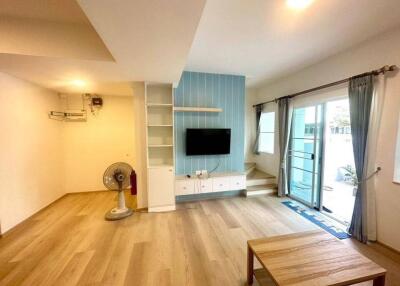 Bright living room with wooden floors, a wall-mounted TV, and large window leading to outdoor space