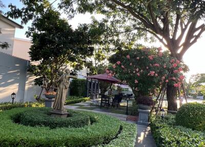 Beautiful garden with manicured hedges, statue, and outdoor seating area under large trees