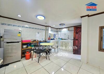 Bright kitchen with white tiles, dining table, refrigerator, and wooden cabinet.