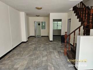 Spacious living area with tiled floor and wooden staircase.