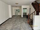 Spacious living area with tiled floor and wooden staircase.