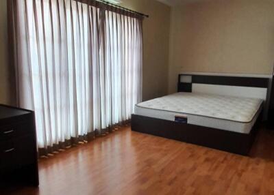 Spacious bedroom with wooden flooring, large window with curtains, air conditioning, dresser, and a bed