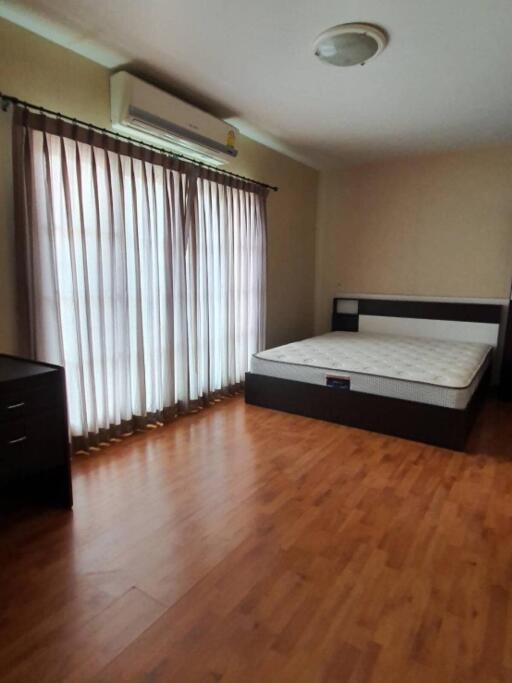 Spacious bedroom with wooden flooring, large window with curtains, air conditioning, dresser, and a bed