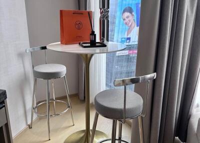 Modern dining area with a small round table and two stylish stools by a window with a city view.