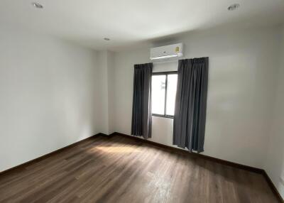 Spacious bedroom with hardwood flooring, window with curtains, and air conditioning unit