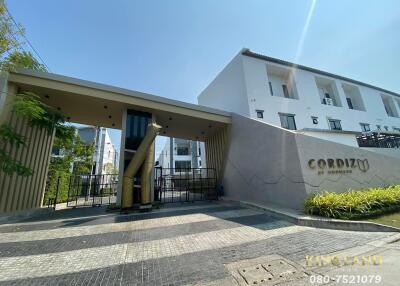 Entrance of a modern residential building named CORDIZ with landscaping and a security gate