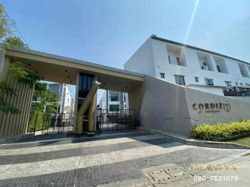 Entrance of a modern residential building named CORDIZ with landscaping and a security gate