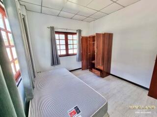 A bedroom with a bed, windows with curtains, and a wooden wardrobe