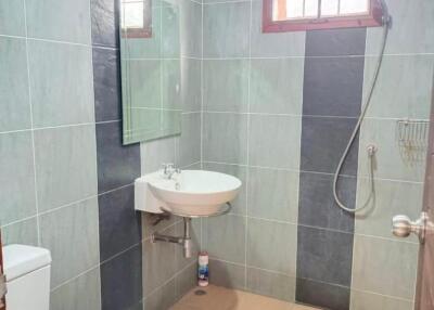 Modern bathroom with tiled walls and floor, featuring a shower area and a mounted sink