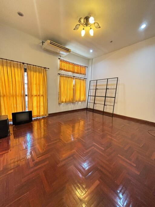 Spacious living room with wooden flooring, bright curtains, and ceiling lighting