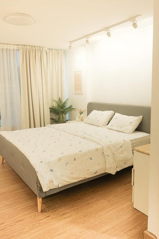 Modern bedroom with a king-size bed, white curtains, and wooden floor