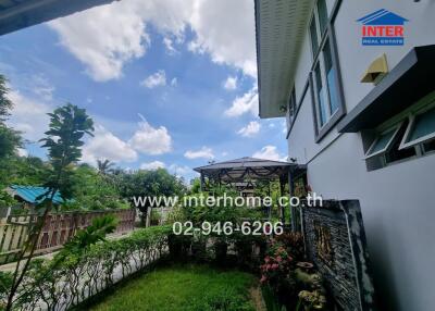 View of a garden area beside a house with a pathway, canopy, and greenery