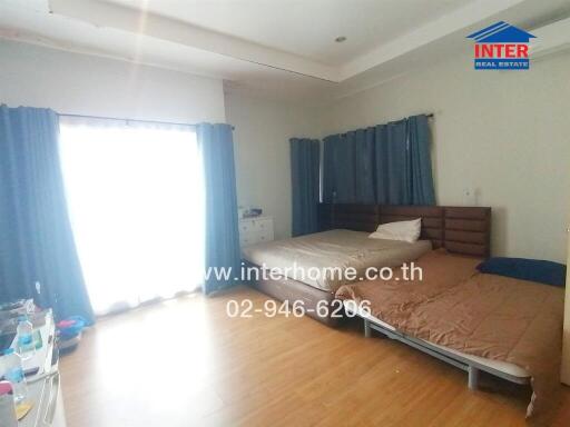 Spacious bedroom with two beds, large window with curtains, and wooden floor