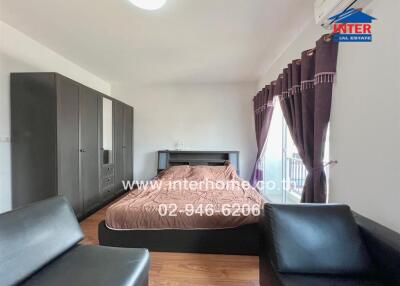 Bedroom with bed, wardrobe, black leather seating, and purple curtains.