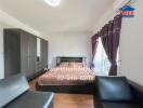 Bedroom with bed, wardrobe, black leather seating, and purple curtains.