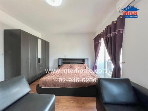 Bedroom with bed, wardrobe, black leather seating, and purple curtains.