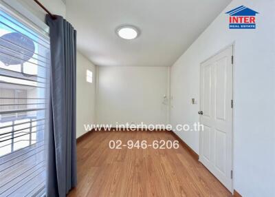 Bright empty bedroom with wooden floor, white walls, and a window with gray curtains.