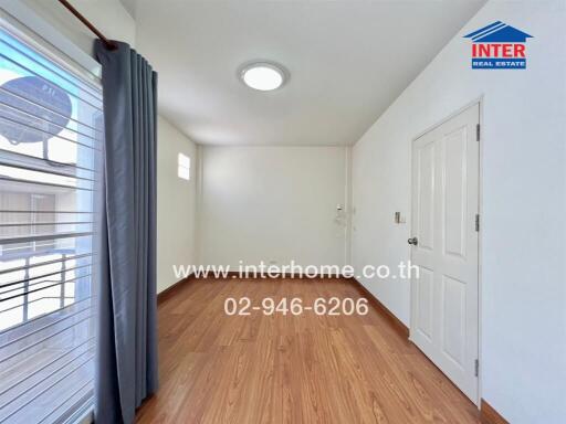 Bright empty bedroom with wooden floor, white walls, and a window with gray curtains.