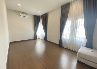 Spacious living room with wooden floor, large windows, curtains, and air conditioning unit