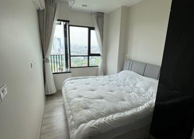 A modern bedroom with large windows offering city views.