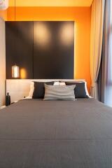 Modern bedroom with minimalist decor featuring a bed with dark bedding, accent pillows, and bright orange walls.