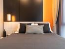 Modern bedroom with minimalist decor featuring a bed with dark bedding, accent pillows, and bright orange walls.