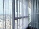 View of cityscape through large windows with sheer curtains