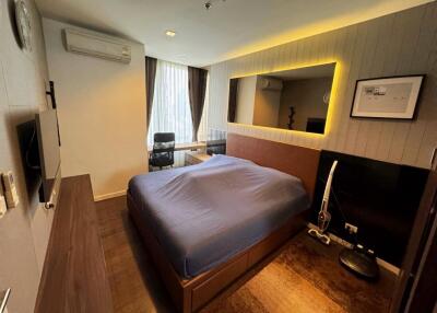 Modern bedroom with blue bedding, wall-mounted TV, large mirror and desk area by the window