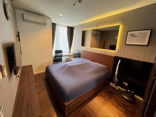 Modern bedroom with blue bedding, wall-mounted TV, large mirror and desk area by the window