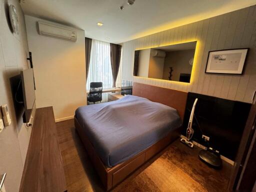 Modern bedroom with blue bedding, wall-mounted TV, large mirror and desk area by the window