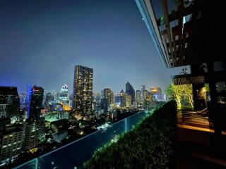 Stunning night cityscape view from a rooftop terrace with greenery and seating area