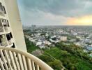 View from a high-rise apartment balcony showing a cityscape with greenery and buildings under a cloudy sky