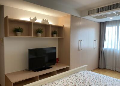 Bedroom with wooden furniture, TV, built-in storage, and window with curtains