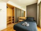 A modern bedroom with a single bed, wooden floor, open closet, desk with chair, and large window.