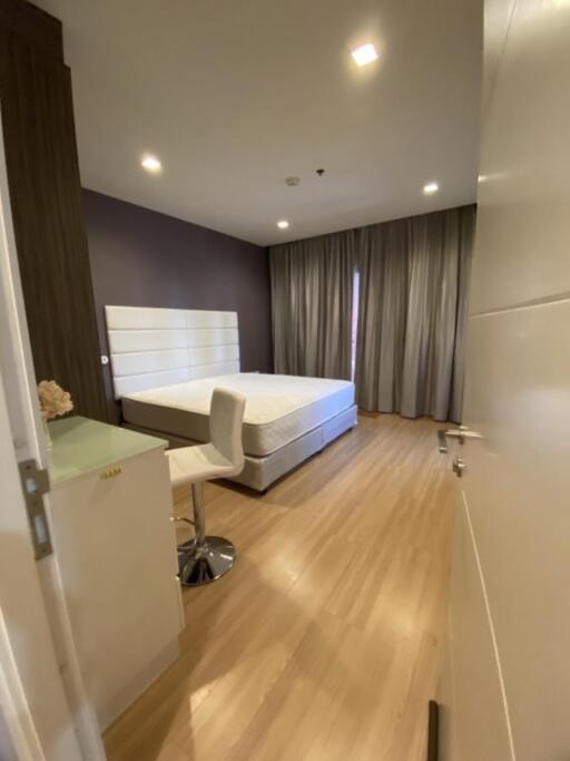 Modern bedroom with wooden flooring, bed, chair, and desk