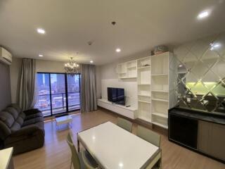 Modern living room with TV, large windows, dining table, and built-in shelving.