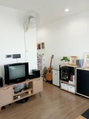 Cozy living room with a TV, wooden flooring, and a guitar