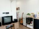 Cozy living room with a TV, wooden flooring, and a guitar