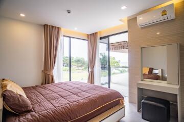 Cozy bedroom with large windows, brown bedspread, and vanity area