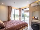 Cozy bedroom with large windows, brown bedspread, and vanity area