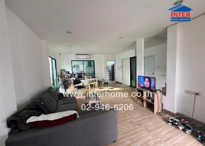 Spacious living room with wooden flooring, a couch, TV, and a dining area in the background