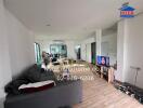 Spacious living room with wooden flooring, a couch, TV, and a dining area in the background