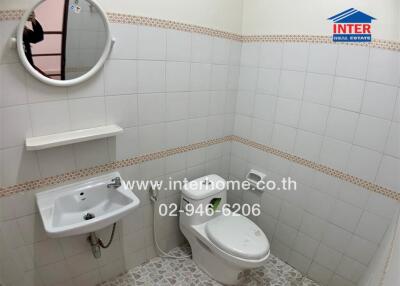 Bathroom with tiled walls and flooring, featuring a toilet, sink, and a mirror.