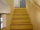 Interior staircase with yellow steps and wooden handrail