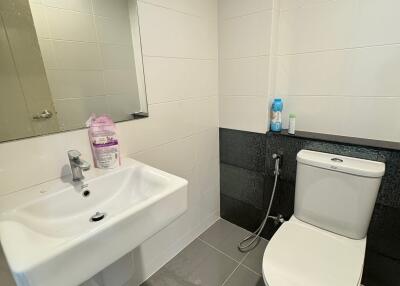 Modern bathroom with tiled walls and floor, featuring a sink, toilet, and mirror.