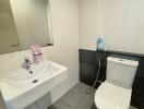 Modern bathroom with tiled walls and floor, featuring a sink, toilet, and mirror.