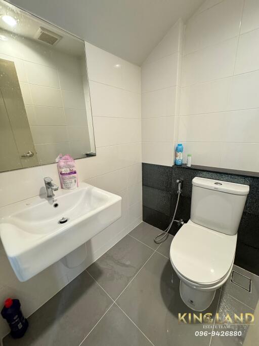 Modern bathroom with tiled walls and floor, featuring a sink, toilet, and mirror.