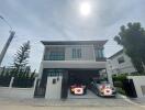 Front view of a modern two-story house with a gated driveway and two cars parked.