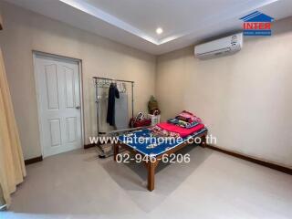 Spacious bedroom with clothes rack, air conditioner, and neatly arranged bed with folded clothes